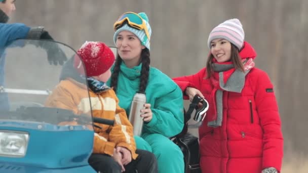 El invierno. Familia en ropa colorida sentada en la moto de nieve, hablando y bebiendo bebidas calientes del termo . — Vídeos de Stock