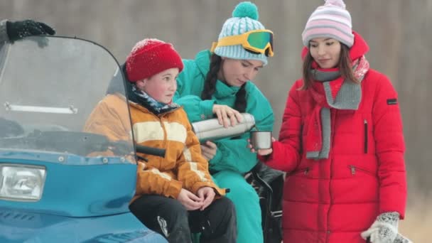 El invierno. Familia feliz con ropa colorida sentada en la moto de nieve y bebiendo bebidas calientes del termo. Un niño riéndose — Vídeo de stock