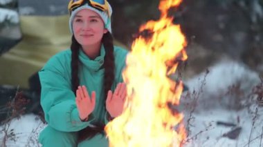 Kış orman. Genç bir kadın oturuyor ve şenlik ateşi tarafından ısınma