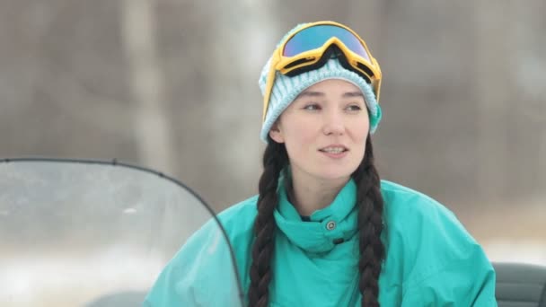 Winter. A young woman in blue down jacket talking while sitting on the snowmobile — Stock Video