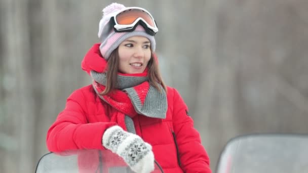 El invierno. Una joven de chaqueta roja se apoya sobre la moto de nieve con una mano — Vídeo de stock