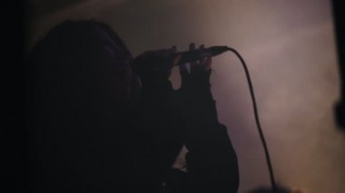 Bir kadın vokal duygusal bir mikrofon tutan bir dumanlı sahnede şarkı söylüyor