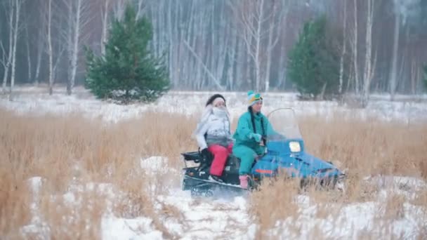 Jonge mensen rijden een sneeuwscooters in een forest van de winter onder de bevroren gras — Stockvideo