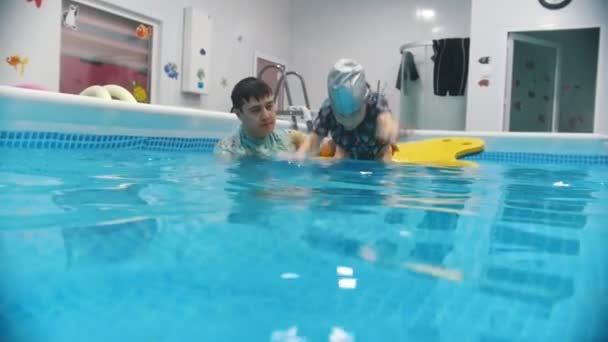 Procedimento de reabilitação de água com criança com paralisia cerebral. Um garoto mergulha na água e pega um brinquedo do fundo da piscina . — Vídeo de Stock