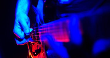 Rock konseri. Gitarist gitar çalıyor. Parlak neon ışıklarla aydınlatılmış gitar. El yakın çekim