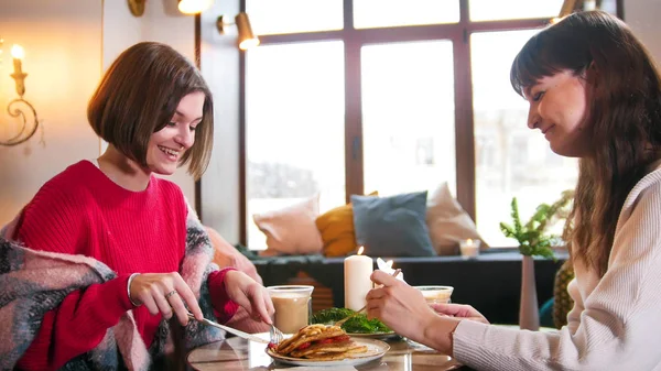 Två unga leende kvinna sitter i modernt kafé och att ha en frukost. Pannkakor och kaffe — Stockfoto