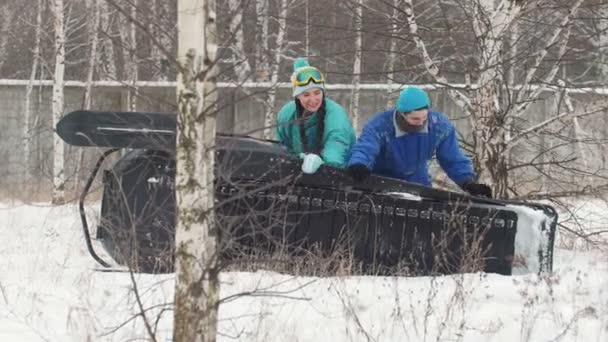 El invierno. Un joven hombre y una mujer volteando la moto de nieve volcada — Vídeos de Stock