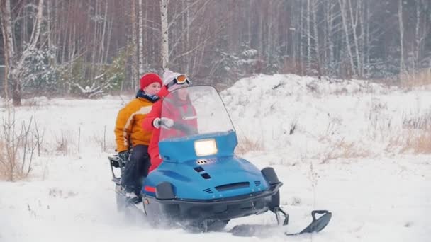 Winter. Een gelukkige jonge vrouw met kleine jongen in kleurrijke jassen rijden op een sneeuwscooter — Stockvideo