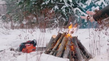 Şenlik ateşi. Kış orman tutuşturulmuş yangında. Bir kişi bir ateşin yanında oturur ve ellerini ısıtır. Yerde yatan bir chainsaw