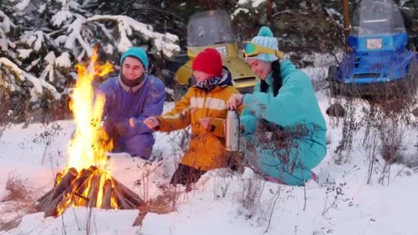 冬天的森林。一家人坐在炉火旁的树林里, 白天说话, 炒香肠 — 图库视频影像