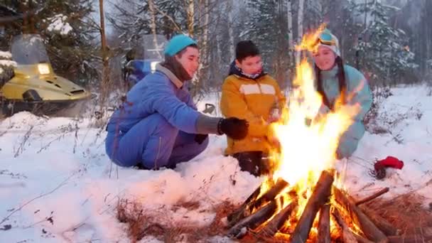 Kış orman. Ormanda ateşin yanında oturan aile. Kızartma sosis şiş üzerinde — Stok video