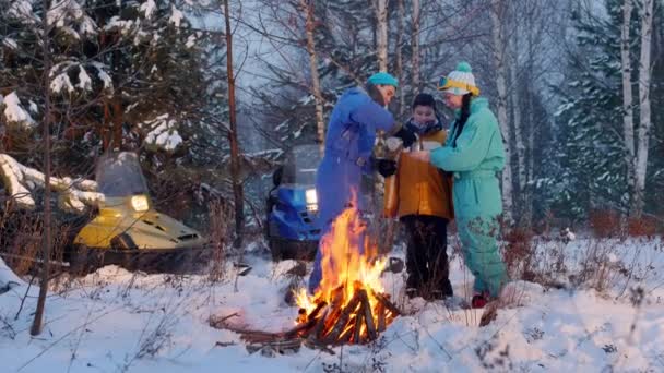 Vinter skog. Familjen stående i skogen vid elden. En ung man spilla te i termos cup — Stockvideo
