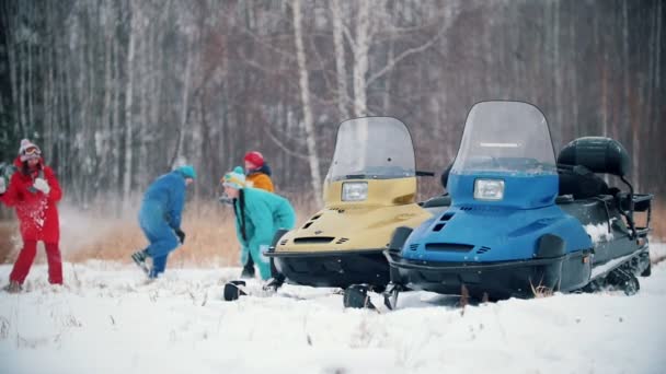 Forêt d'hiver. Famille en vêtements colorés s'amuser à jouer aux boules de neige près des motoneiges. Mouvement lent — Video