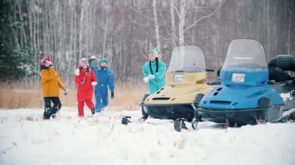 Bosque de invierno. Familia feliz en ropa colorida jugando bolas de nieve cerca de las motos de nieve. Corriendo hacia la cámara. Movimiento lento — Vídeo de stock