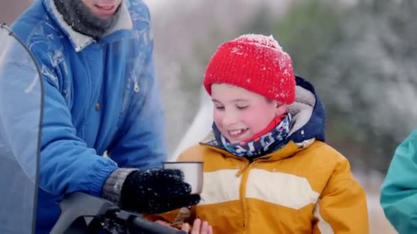 Winterwald. junge Familie in bunten Kleidern, die sich neben dem Schneemobil ausruhen. im Kreis eine Tasse mit Heißgetränk — Stockvideo
