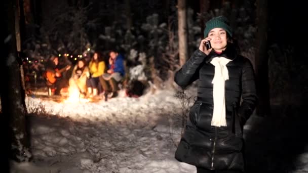 Jóvenes en el bosque invernal. Una joven se alejó del grupo para hablar por teléfono. — Vídeo de stock