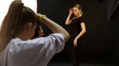 Genç kadın modelinde bir fotoğraf oturumu stüdyoda. Model siyah giysilerle çekim. Fotoğrafçı flash kullanır