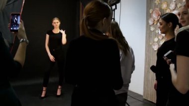 Genç kadın modelinde bir fotoğraf oturumu stüdyoda. Model siyah giysilerle çekim. Tam yüksekliği çekim. Başka bir modelleri üstünde onların telefon çekim