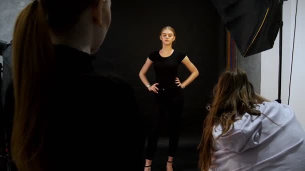 स्टूडियो में फोटो सत्र रखने वाली युवा महिला मॉडल। काले कपड़ों में मॉडल की शूटिंग। पूरी ऊंचाई में शूटिंग — स्टॉक वीडियो