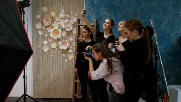 Молодая женщина-модель проводит фотосессию в студии. Фотограф снимает, пока другие модели делают селфи — стоковое видео