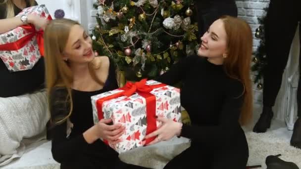 İki genç kadın modelleri bir büyük tatil kutu kırmızı kurdele ile tutarak un üzerinde oturuyor. Hediyeler vererek. Mutlu — Stok video
