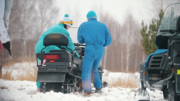 Jóvenes con ropa brillante preparando la moto de nieve — Vídeo de stock