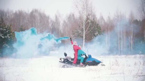 冬天的森林。年轻人乘坐雪地摩托。一个拿着蓝色烟雾弹的女人。蓝色的烟雾开心 — 图库视频影像