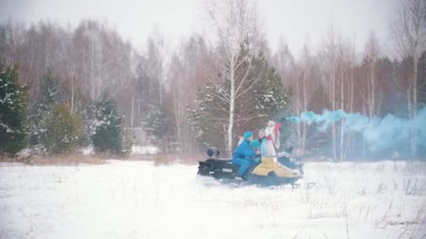 Bosque de invierno. Jóvenes montando motos de nieve. Una mujer sosteniendo una bomba de humo azul — Vídeos de Stock