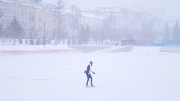 Молода жінка катається на ковзанах на відкритому ковзанах надворі. Сильний снігопадweather condition — стокове відео