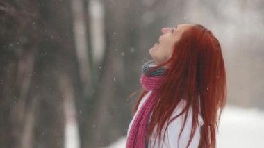 Winter park. Kaldırımda parlak kırmızı saç ayakta olan bir kadın. Kar taneleri ağızlı yakalamak