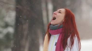 Winter park. Kaldırımda parlak kırmızı saç ayakta olan bir kadın. Kar taneleri ağızlı yakalamak. Ağır çekim