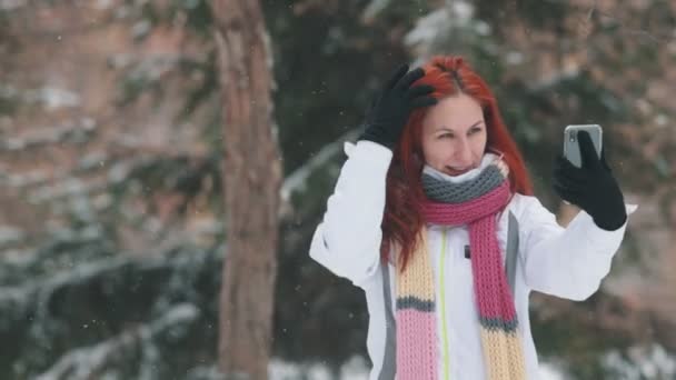 Winter park. Μια γυναίκα με τα φωτεινά κόκκινα μαλλιά στέκεται μπροστά από χιονισμένα δέντρα και να αγγίζει τα μαλλιά της — Αρχείο Βίντεο