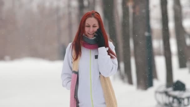 Parque de invierno. Una mujer sonriente con el pelo rojo brillante hablando por teléfono — Vídeos de Stock