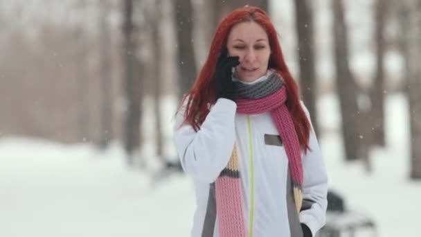 Parque de Inverno. Uma mulher com cabelo ruivo brilhante a falar ao telefone. Uma forte queda de neve. Fechar — Vídeo de Stock