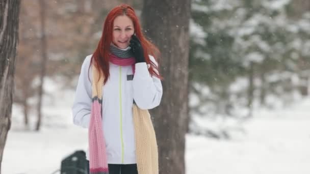 Winter park. Egy mosolygó nő csillogó vörös hajú beszél telefonon. Nevetve — Stock videók