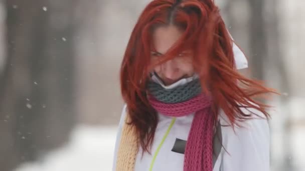 Winter park. Een vrouw met fel rood haar staande op de stoep. Wapperend haar en vangen van sneeuwvlokken met een mond. — Stockvideo