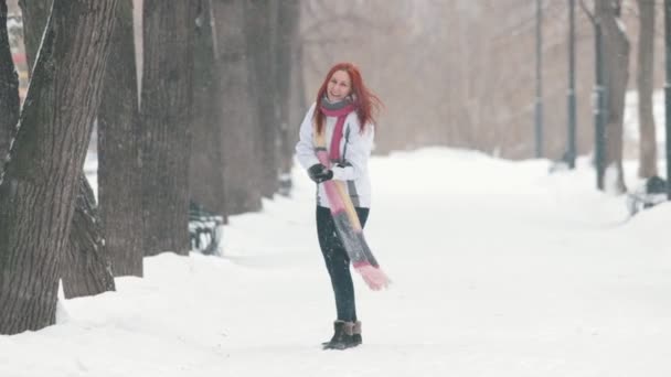 Parque de Inverno. Uma mulher alegre com cabelo vermelho brilhante em pé na calçada, fazendo uma bola de neve e jogando-a para a frente — Vídeo de Stock