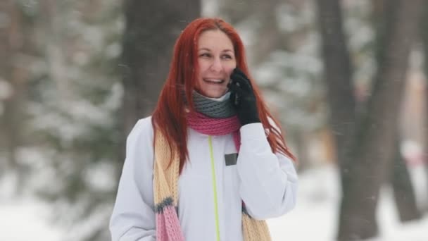Зимний парк. Женщина с ярко-рыжими волосами говорит по телефону. Сильный снегопад. Портрет — стоковое видео