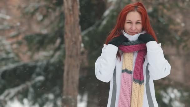 Winter park. Μια χαρούμενη γυναίκα με φωτεινά κόκκινα μαλλιά προσπαθεί να ζεσταθεί σε κρύο καιρό — Αρχείο Βίντεο