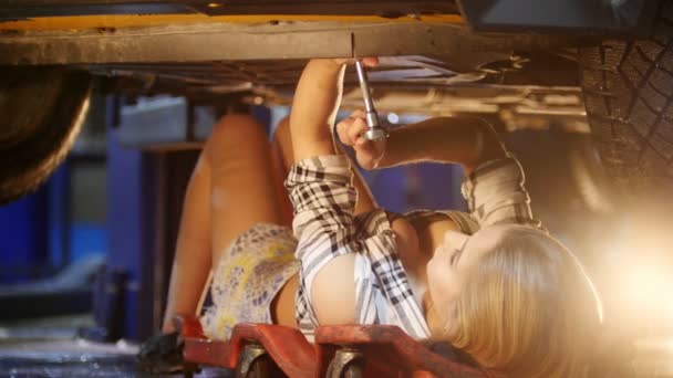 Autószervíz. Fiatal nő szexi alakja az autó alatt fekvő és rögzítő ez. Szerkezet-val egy csavarkulcs
