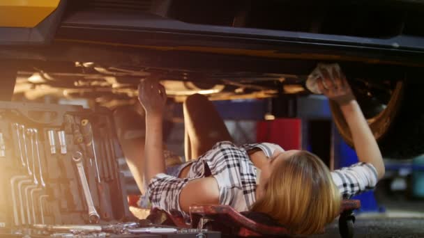自动服务。年轻性感的女人躺在车底, 用抹布擦拭它 — 图库视频影像