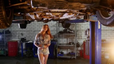 Araba tamir servisi. Bir araba Asansör. Genç seksi kadın arabanın altına girer ve onun üzerine asılı ayrılamıyorum