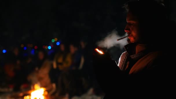 Skäggig man stående i vinter skog på natten och lysa upp cigaretten — Stockvideo