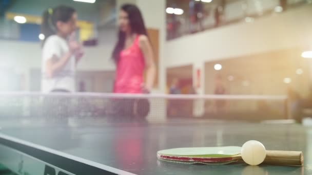 Ping pong hrát. Mladé ženy mluví na pozadí. Raketa a míček na popředí — Stock video