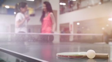 Ping pong bir spor klübünde oynamaktadır. Arka plan üzerinde konuşan genç kadın arkadaşlar. Ön plan üzerinde küçük top ve raket
