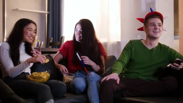 Fyra unga glada människor sitter i soffan och tittar på Tv tillsammans — Stockvideo