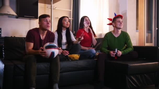 Cuatro jóvenes sentados en el sofá y viendo el partido de fútbol. Un equipo golpea el gol, los fans están felices y un hombre decepcionado — Vídeos de Stock