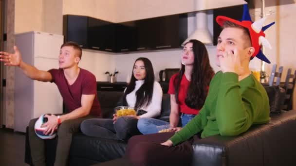 Des amis passent du temps ensemble. Quatre jeunes assis sur le canapé et s'amusant à regarder le match de football. Homme excité debout et se réjouit pour l'équipe — Video