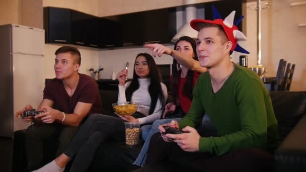Vier jongeren hebben een goede tijd samen, twee jonge man speelspel terwijl hun vriendinnen praten over het spel — Stockvideo
