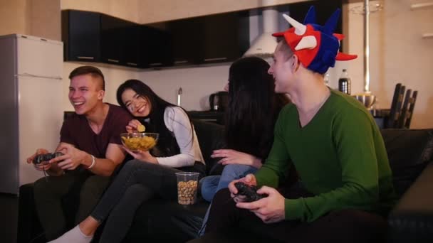 Двое молодых людей играют в игру, пока их подружки разговаривают за игрой — стоковое видео
